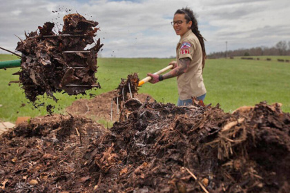 female turning compost pile with pitchfork