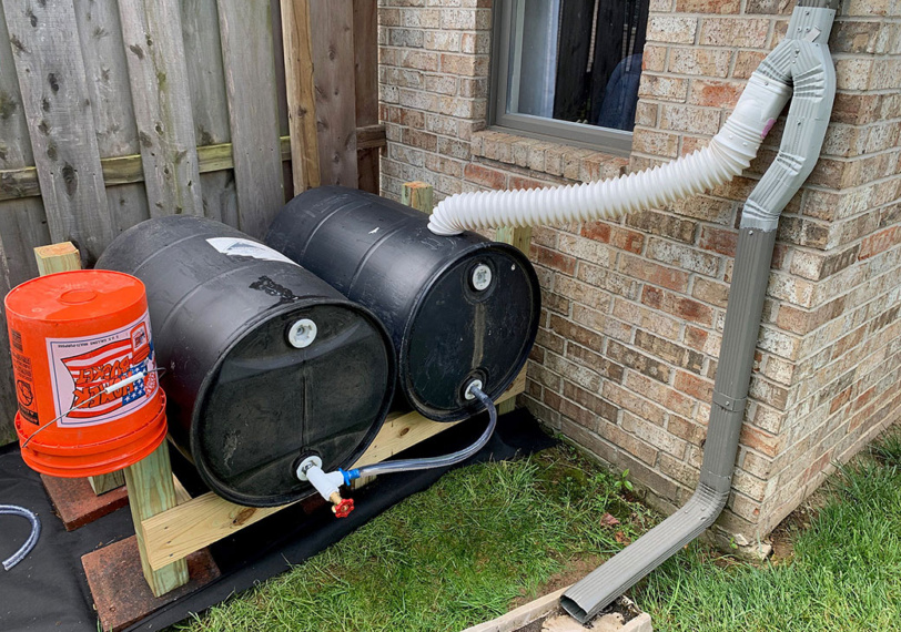 two horizontal rain barrels next to a house