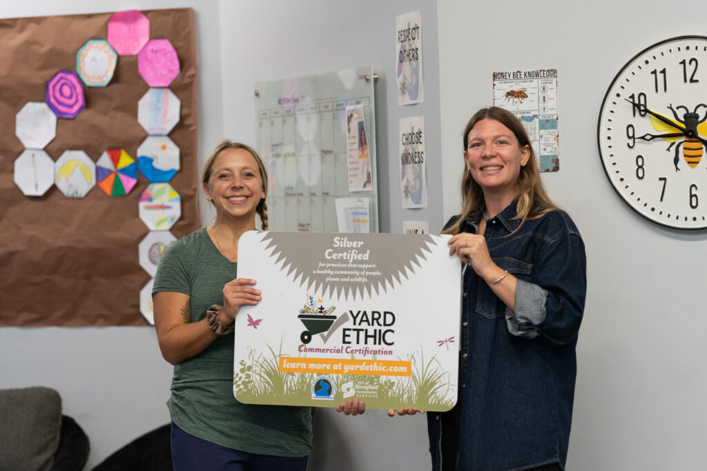 Environmental Services Employee Sarah Wilkerson and Summit Prep Teacher Elise Bowsher holding the Silver Certified Yard Ethic Commercial Certification sign.