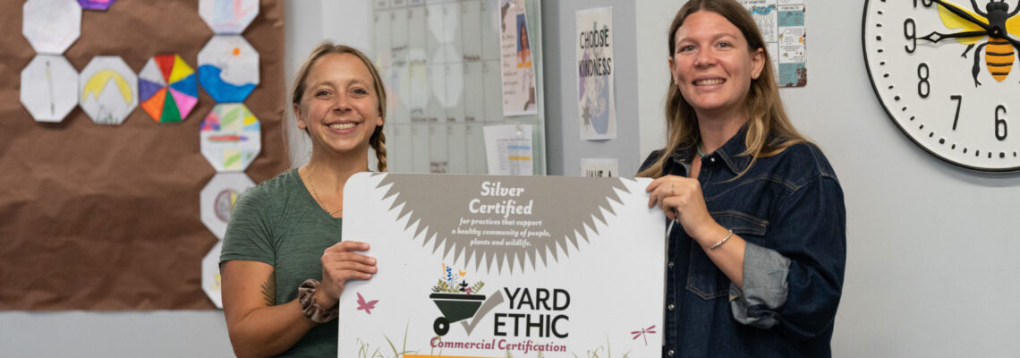 Environmental Services Employee Sarah Wilkerson and Summit Prep Teacher Elise Bowsher holding the Silver Certified Yard Ethic Commercial Certification sign.